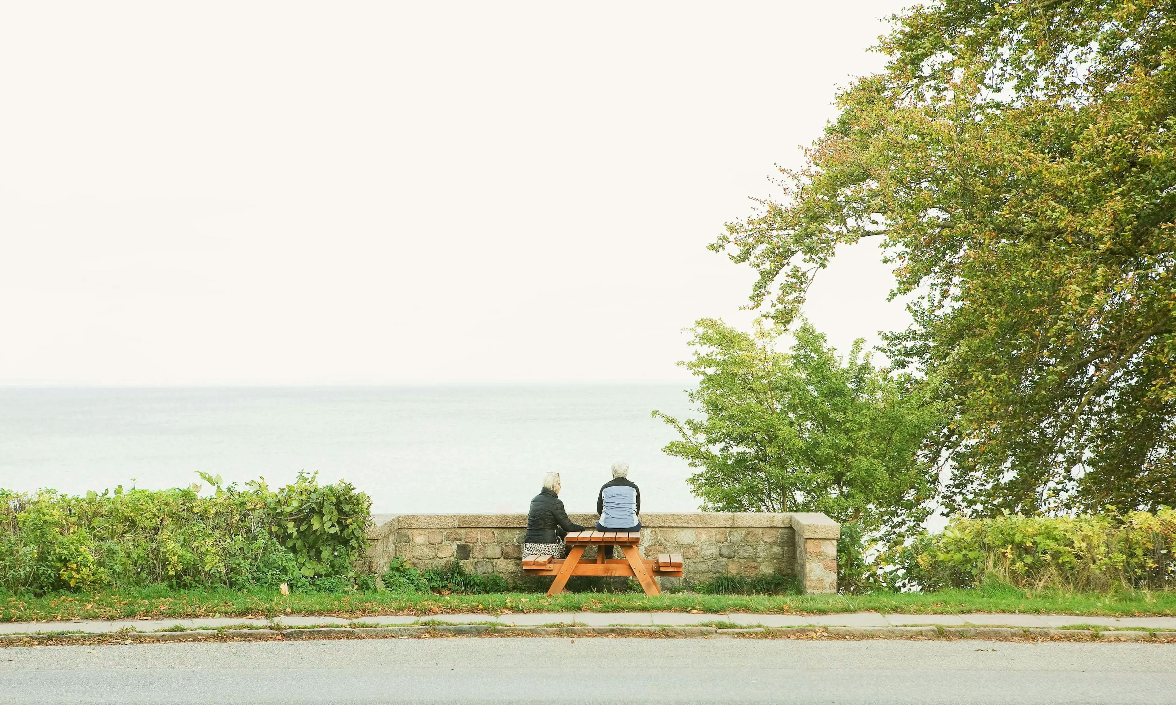 A photo of two elderly individuals engaged in conversation while seated on a bench.