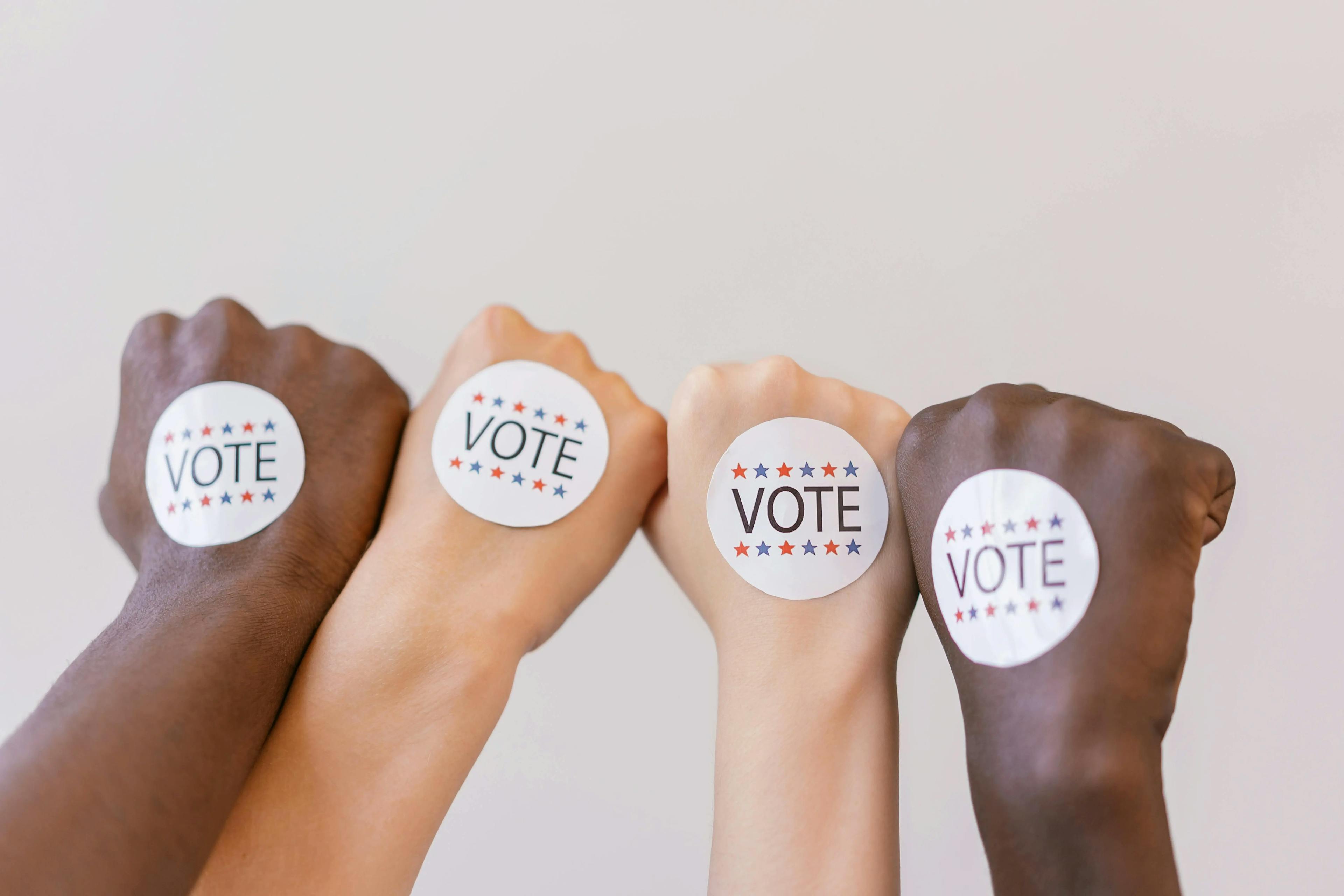 A close-up of closed fists with a sticker that says "vote".